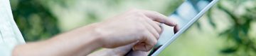 Person touches electronic notebook with forefinger, trees in background