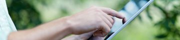 Person uses forefinger on electronic notebook, trees in background