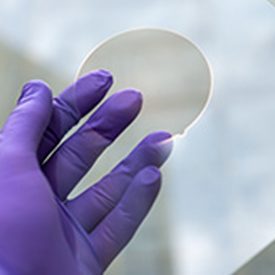 Hand in purple lab glove touches round hole in glass