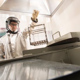 Man in protective suit holds metal, glass container over vat